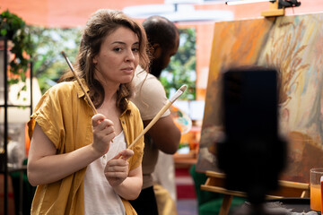 Woman painter filming demonstration during artistic creative process and explaining the painting technique used for an online e learning tutorial. Diverse team creating a vlog for virtual classroom.