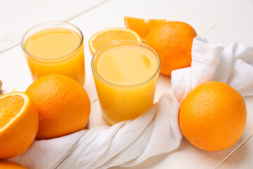 Glasses of tasty juice with fresh oranges on white wooden background