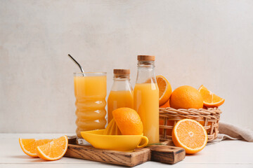 Oranges with juicer, glass and bottles of tasty juice on white wooden table
