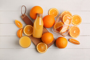 Oranges with glass and bottle of tasty juice on white wooden background