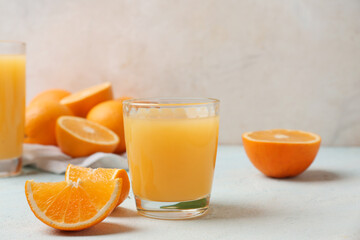 Glass of tasty juice with oranges on light background