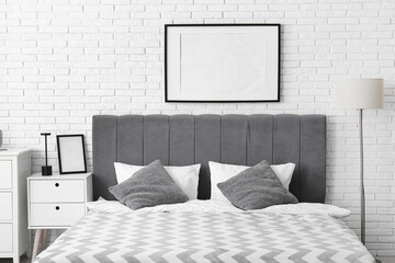 Modern bed and empty poster on white brick wall
