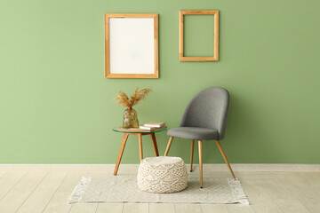 Chair with table, pouf and empty photo frames on green wall