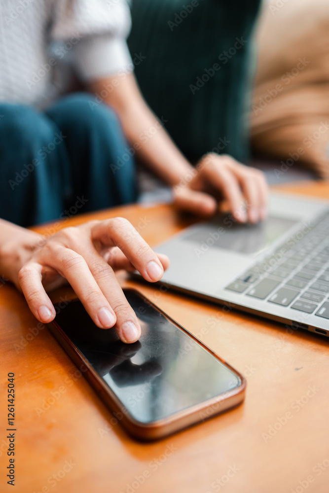 Poster hands interacting with smartphone and laptop, showcasing multitasking and remote work in a cozy sett