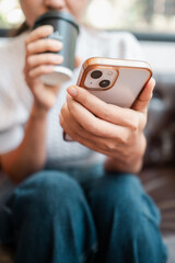 A person in casual attire holds a smartphone while sipping coffee, capturing a moment of relaxation and connectivity.