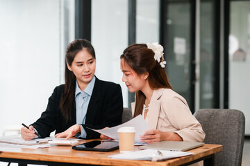 Two women in a business meeting discussing documents in a modern office environment, showcasing teamwork and collaboration.