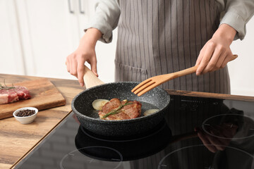 Woman frying tasty steak in kitchen