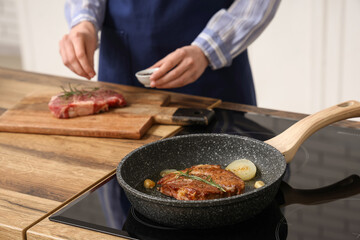 Frying pan with roasted steak on stove in kitchen