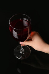 Female hand holding glass of red wine on dark background