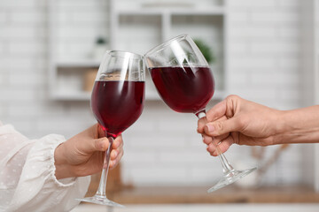 Hands of women clinking glasses of red wine in kitchen