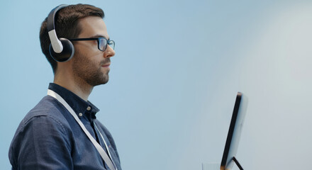 A man wearing glasses and headphones is working on a laptop