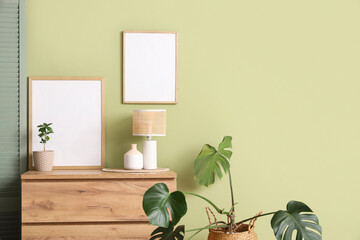 Blank posters on chest of drawers and houseplant near green wall in room