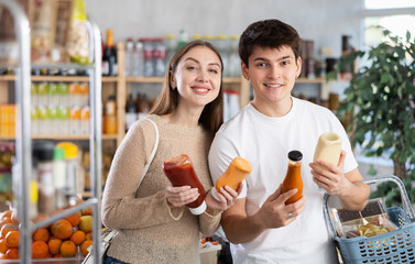 Married young happy couple chooses spicy sauce in big supermarket