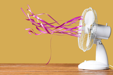 Modern electric fan with pink fluttering ribbons on yellow background