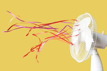 Modern electric fan with colorful fluttering ribbons on yellow background, closeup