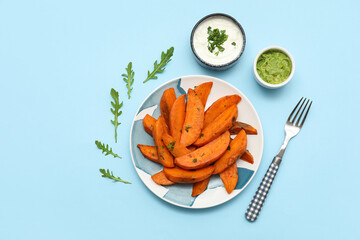 Plate with baked sweet potato, sauces, arugula and fork on blue background