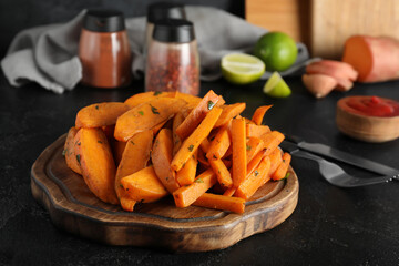 Wooden board with baked sweet potato and cutlery on black grunge background