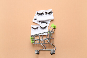 Shopping cart with different false eyelashes on beige background
