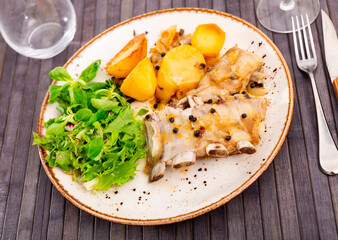 Appetizing grilled pork ribs with vegetable side dish of roasted potatoes garnished with greens and salad on plate. Spanish cuisine
