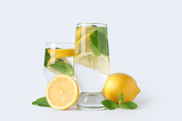 Glasses of water with lemons and mint leaves on white background