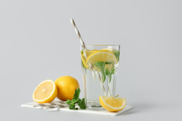 Glass of water with lemon slices, mint leaves and straws on grey background