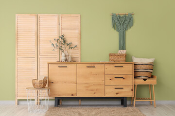 Folding screen, chest of drawers with  eucalyptus branches in vase and decor near green wall in room