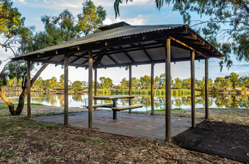 A covered picnic shelter at Wimmera River in Horsham, Victoria, with a deck platform and seating bench, overlooking the calm waters and beautiful environment in a park.