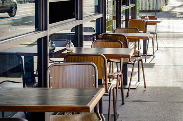 A row of empty tables and chairs at an outdoor cafe or restaurant with wooden furniture at an urban...
