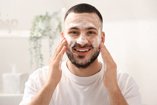 Young man washing his face with soap in bathroom, closeup