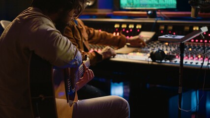 Creative musician singing guitar in professional studio control room, recording his tracks with...