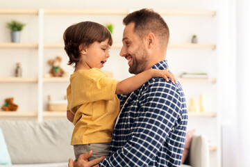 Daddy and son connection. Profile portrait of young happy loving father embracing his adorable little kid, carrying him on hands at home interior