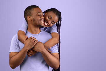 Obraz premium Happy Loving Family Concept. Front portrait of joyful black sweethearts hugging, cheerful lady embracing her man fron behind back, standing together isolated over purple violet background in studio