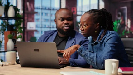 Young couple doing teamwork and multitasking on laptop at desk, fully connected to the internet while managing freelance work and remote responsibilities. Browsing web at home. Camera B.