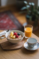 Delicious healthy oatmeal breakfast bowl topped with fresh berries, pineapple, and natural orange juice, served in a cozy, rustic home setting.
