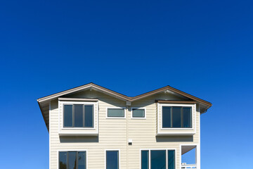 Exterior view of upper floors of contemporary residential building with beige siding, large windows, and a symmetrical design, set against a vibrant, clear blue sky