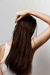 Naklejka premium Hair care, long hair styling, woman combing hair, back view in white tank top, neutral background, healthy hair concept featuring care and grooming routines, personal care focus