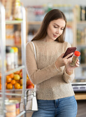 Female shopper scanning QR code on bottle ground pepper label in grocery department of supermarket