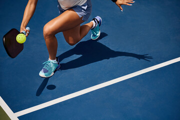 Legs and shadow of a girl playing pickleball on a blue court