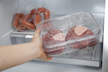 Woman taking frozen beef steaks out of fridge, closeup