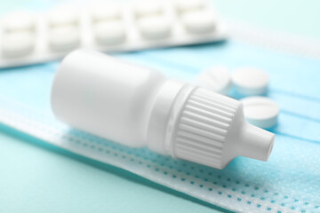 Allergy treatment. Nasal drops, pills and protective mask on light blue background, closeup