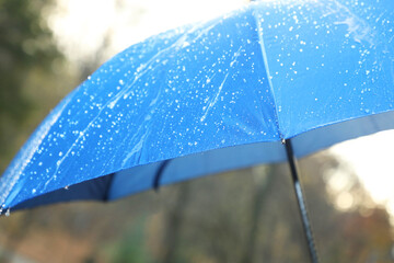 Open blue umbrella under pouring rain outdoors, closeup