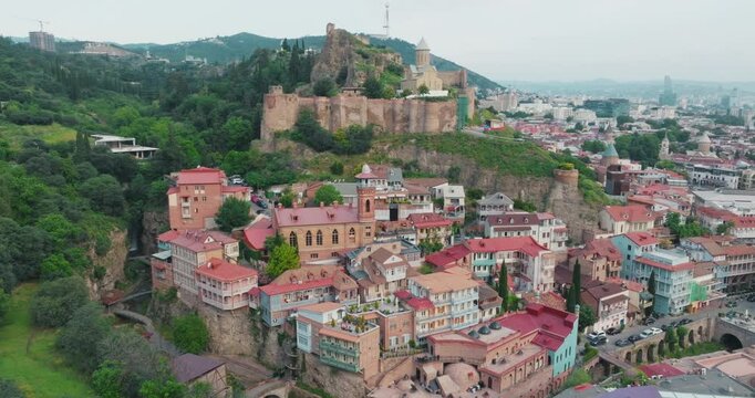 Historical Abanotubani district and Narikala Castle in Tbilisi. Drone view circling around houses and castle with colorful balconies in the foreground.