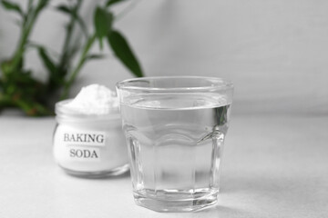 Glass of water and baking soda on white table, selective focus