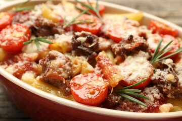 Delicious pasta casserole with cheese, tomatoes, minced meat and rosemary in baking dish on table, closeup