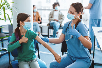Portrait of adolescent patient in protective face mask showing thumbs up gesture after getting...