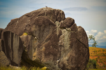 A large rocky outcrop under a partly cloudy sky, with natural surroundings.