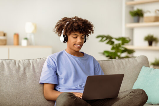 Remote education. Cool black teen guy in headphones having online lesson, participating in webinar on laptop indoors. African American youth studying from home during covid quarantine