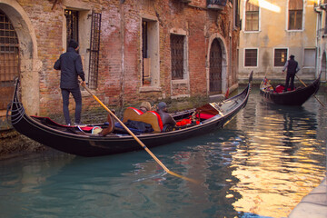 Gondolas navigating through a narrow canal in Venice, Italy, with historic buildings on either side.