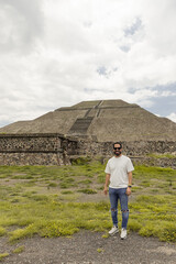 Teotihuacan, Mexico. A Mexican American tourist with a backpack and hat enjoys the view from the top of the Moon Pyramid. The Sun Pyramid and Avenue of the Dead can be seen in the distance.
