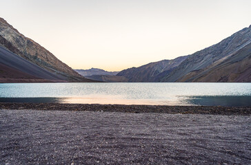 A vast, desolate scene at Embalse El Yeso, Andes Mountains of Chile. Still waters reflect the muted light of the sky. Steep, rugged mountains rise on either side